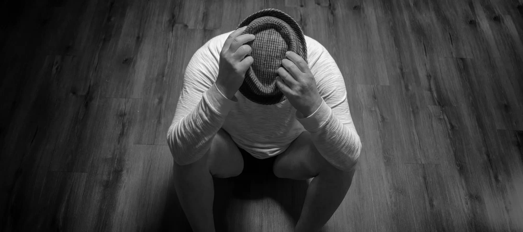 Mann zusammengekauert in trauriger Stimmung und Händen über dem Kopf