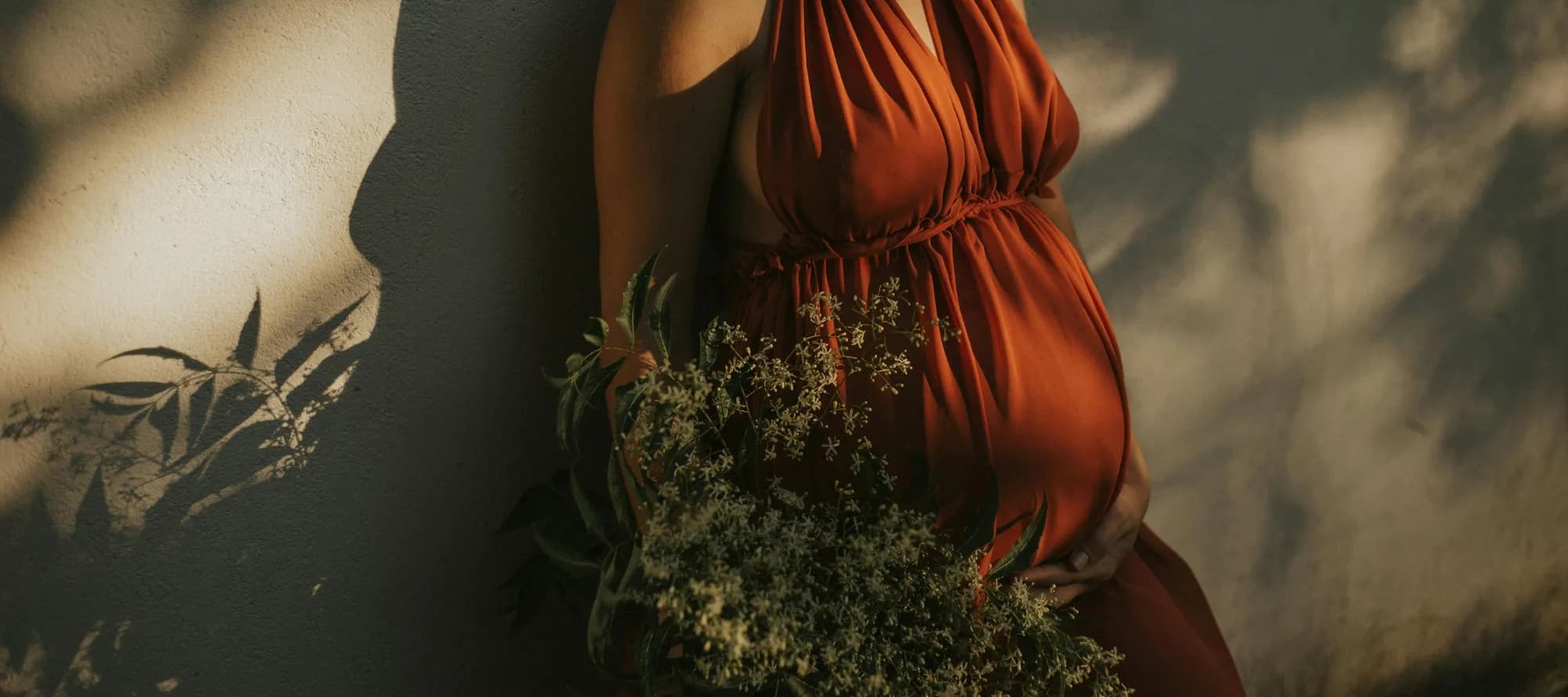 Schwangere in rotem Kleid an Hauswand