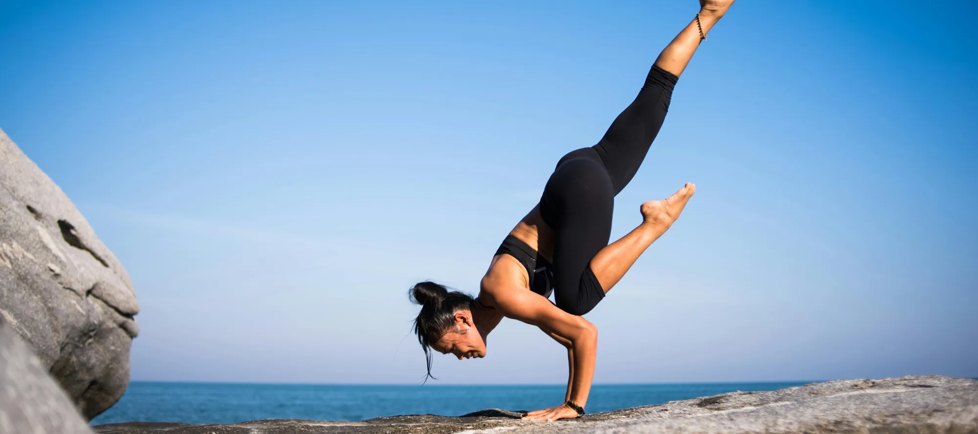 Frau beim Yoga auf Fels am Meer